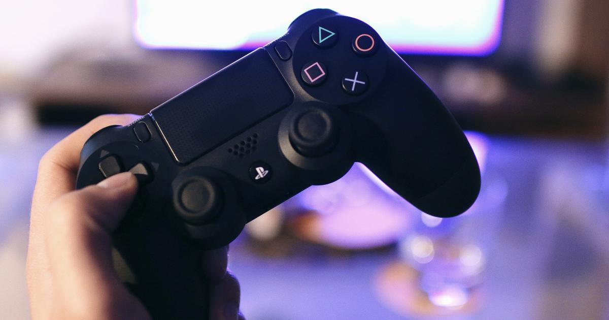Een hand houd een playstation controller vast.
